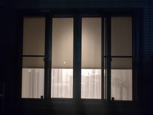 外から見た夜の断熱ハニカムシェードを半分閉めたところ。下側のレースカーテン越しに中がうっすら見える。